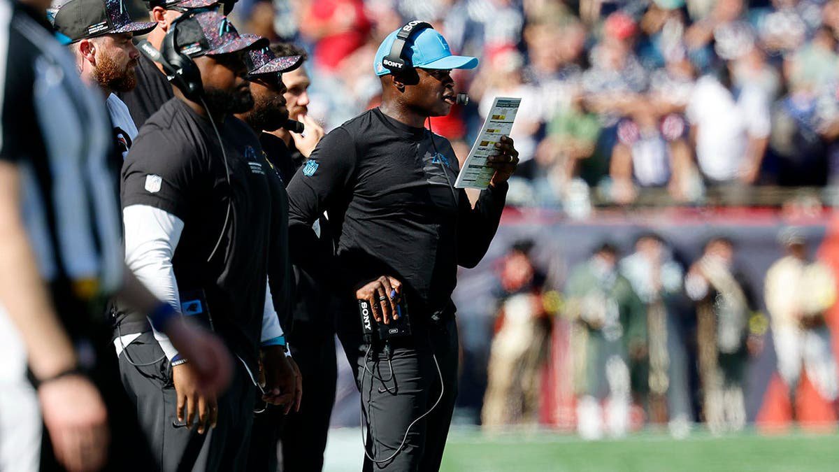Ejiro Evero stands on the sideline during a football game.