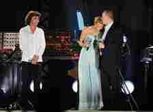 Princess Charlene of Monaco in a blue outfit leaning into Prince Albert II of Monaco appear onstage during the Jean Michel Jarre wedding concert 