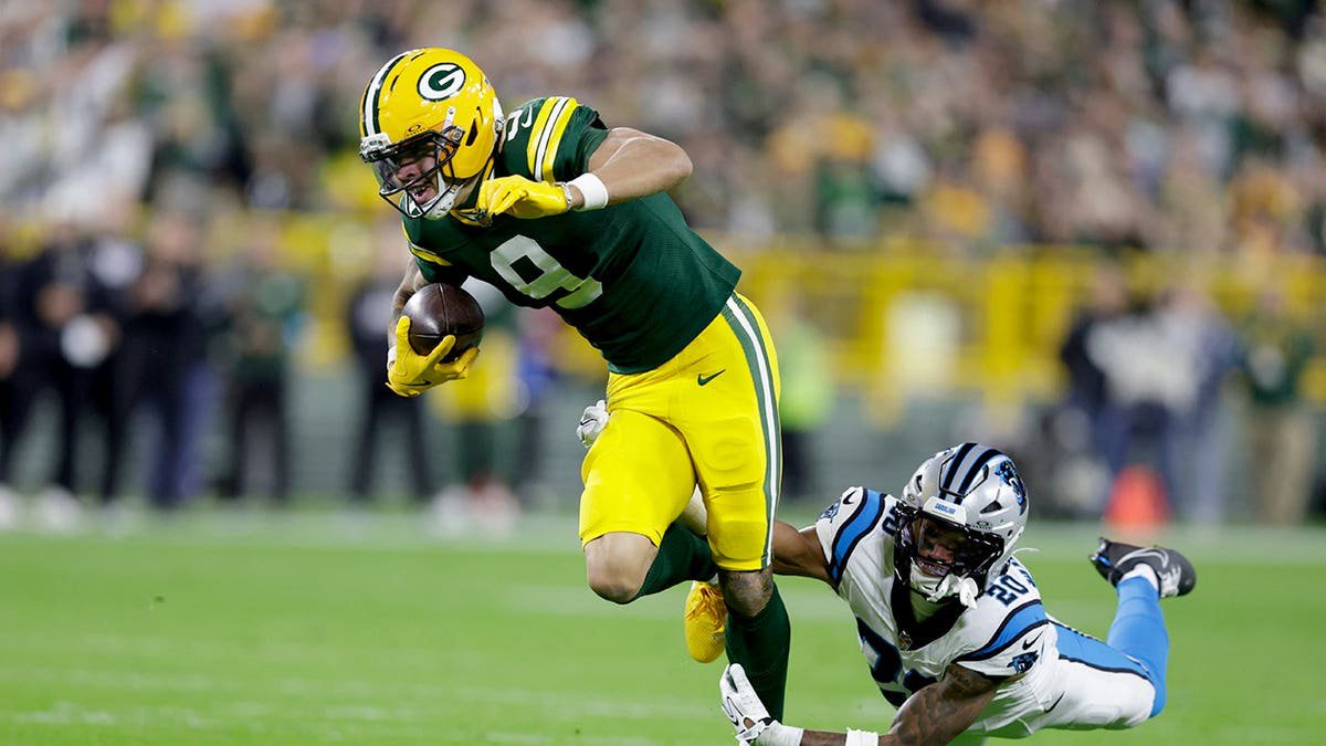 Christian Watson catches a pass while being hit by Zakee Wheatley during an NFL game.