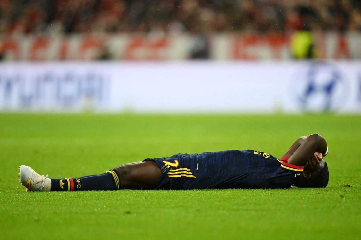 Bukayo Saka lying supine on the pitch and covering his face with both arms during an Arsenal match
