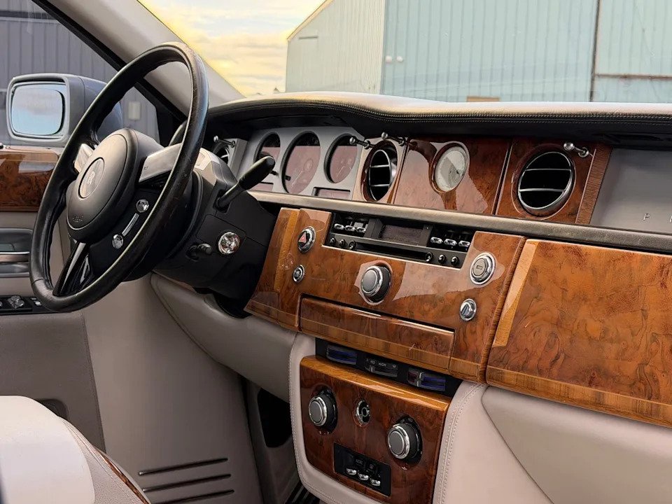 vehicle interior view. Dashboard with wood trim, analog gauges and cream leather surfaces.