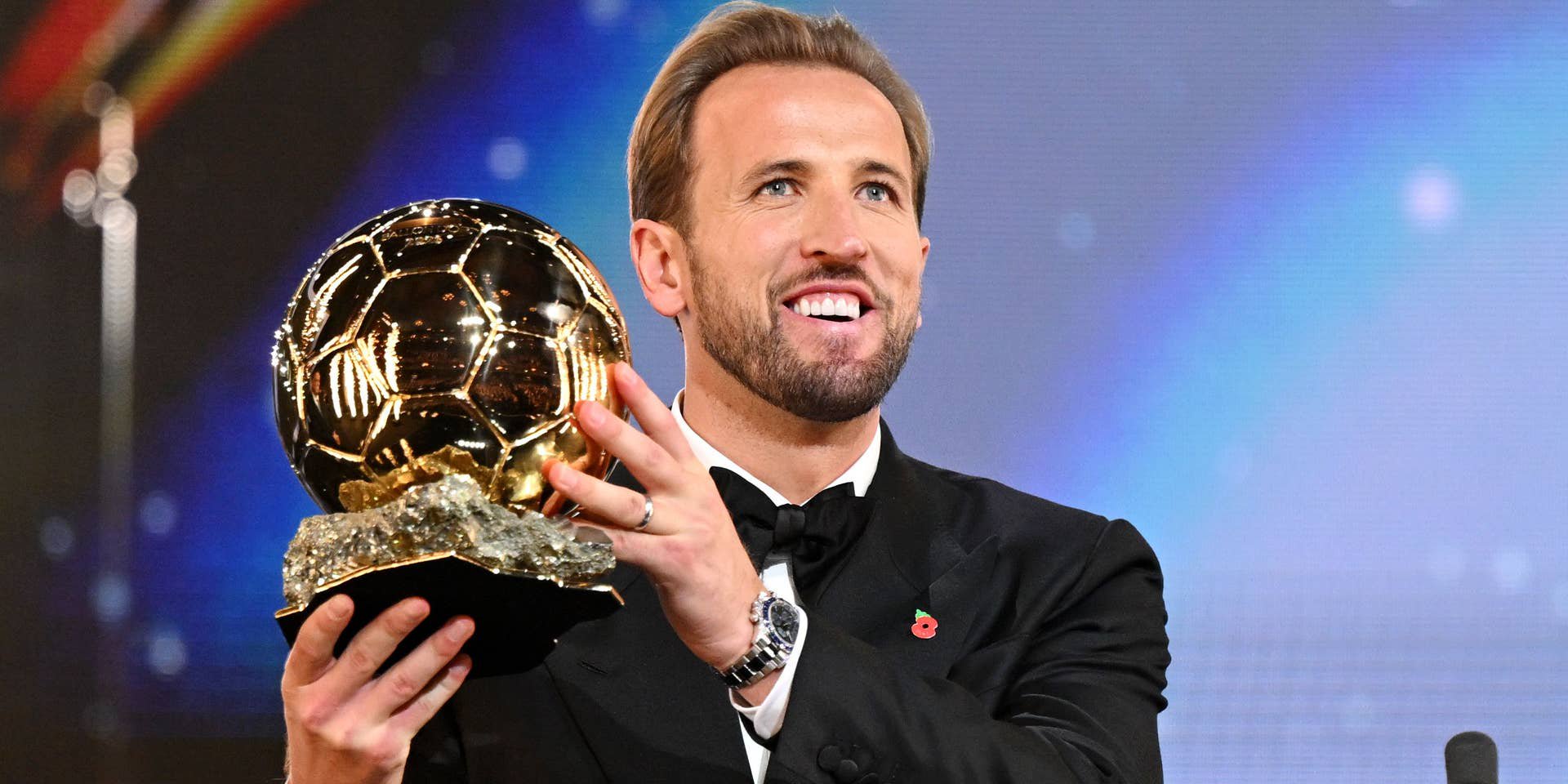 Ein Mann im Anzug hält lächelnd einen goldenen Ballon d'Or-Pokal in die Höhe.