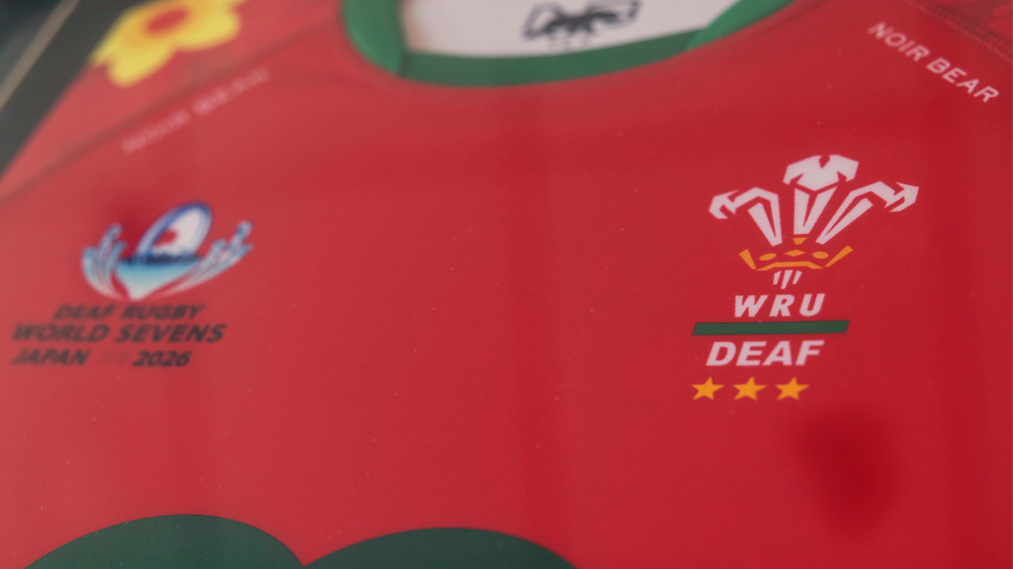 Close-up of a red Wales Deaf Rugby jersey featuring the WRU Deaf crest with three gold stars and the logo for the Deaf Rugby World Sevens Japan 2026 tournament.