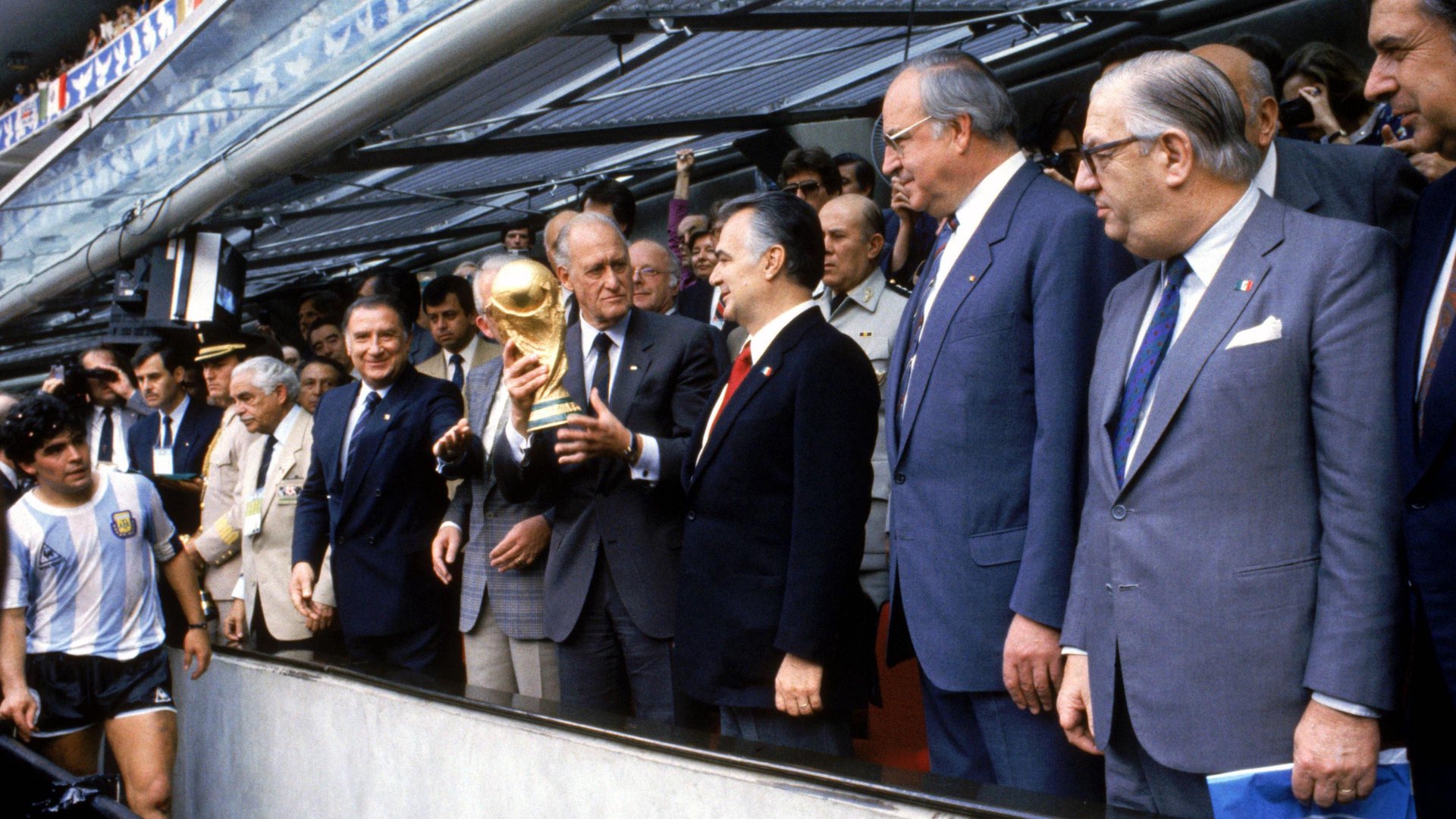 A Peter Robinson image which shows a row of men in suits holding the world cup trophy. Diego Maradona is in the far left of the shot and is looking towards the cup. 