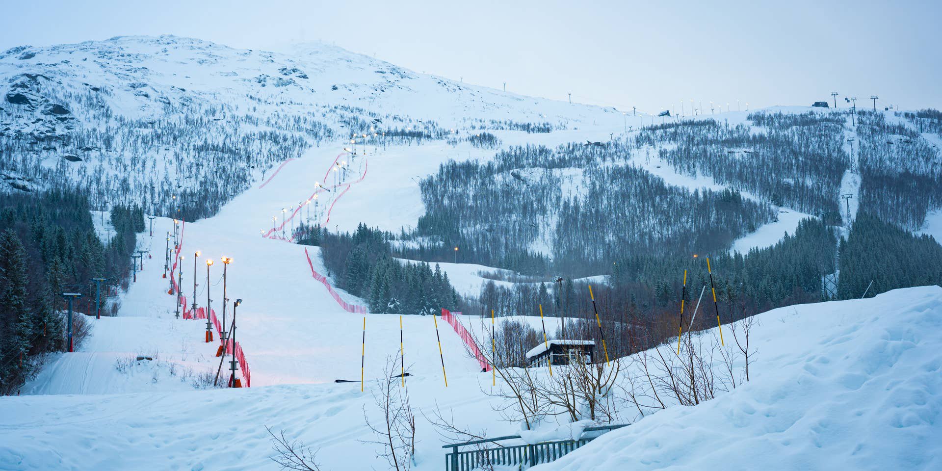 Beleuchtete Skipiste im verschneiten Skigebiet Narvikfjellet in Norwegen, umgeben von Bäumen.