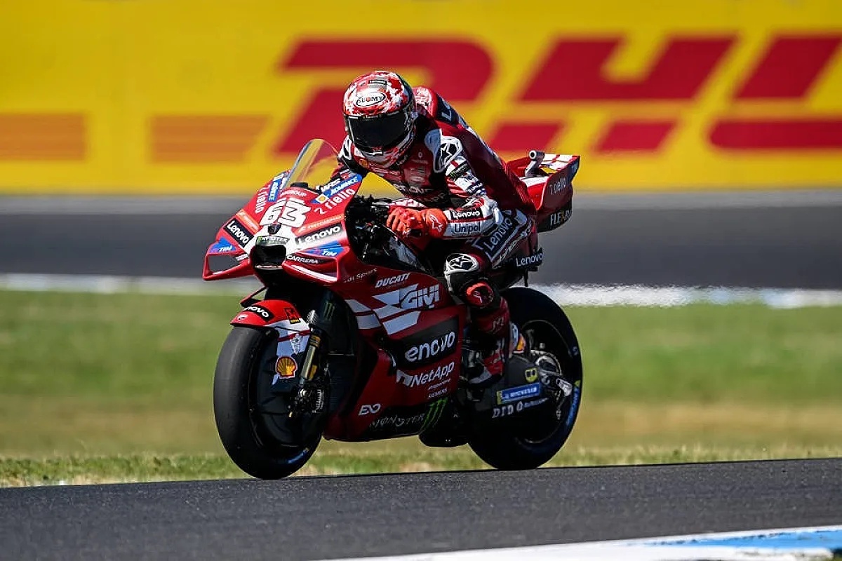 Rider in red Ducati leathers and helmet on a red Ducati Desmosedici GP at a MotoGP track, with a DHL banner behind