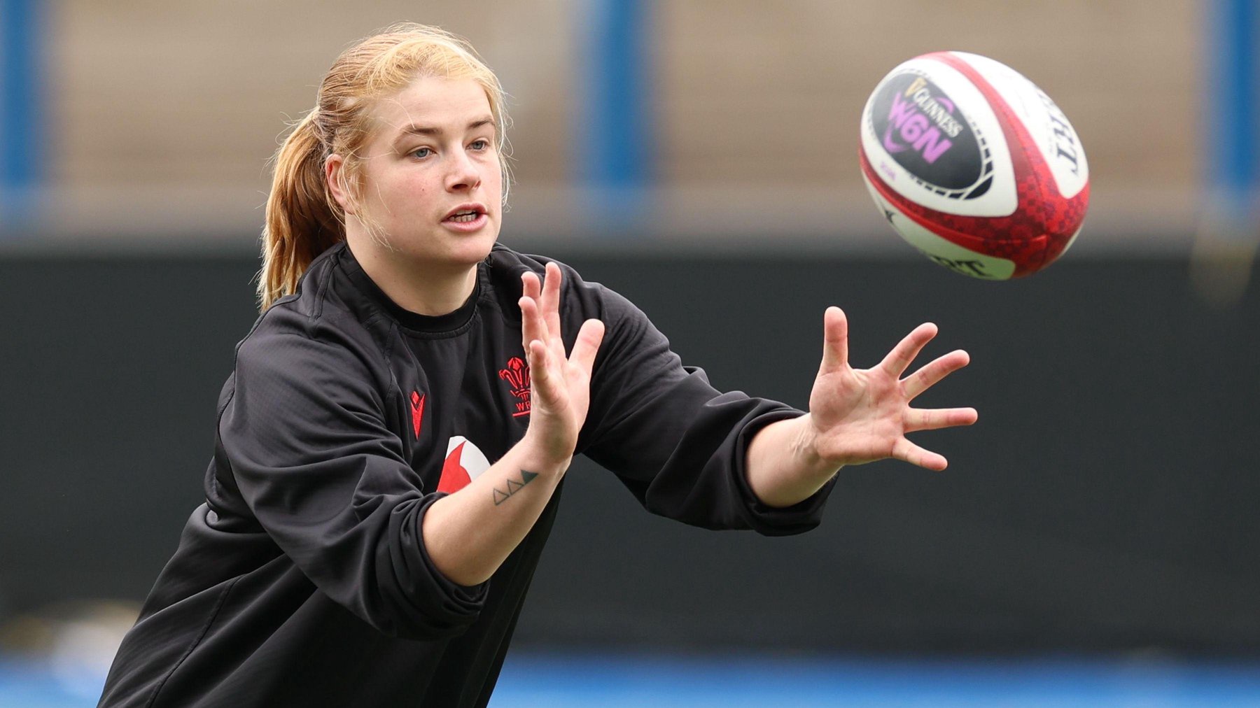 Bethan Lewis in black Wales training top holds her hands forward ready to catch an approaching rugby ball 