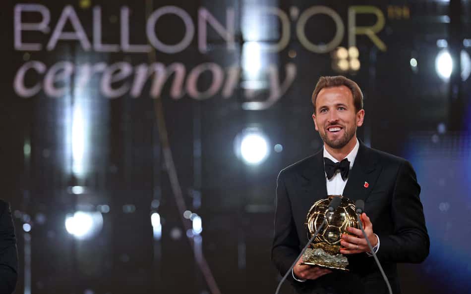 Homem de terno preto no palco segurando o troféu Ballon d'Or na cerimônia.