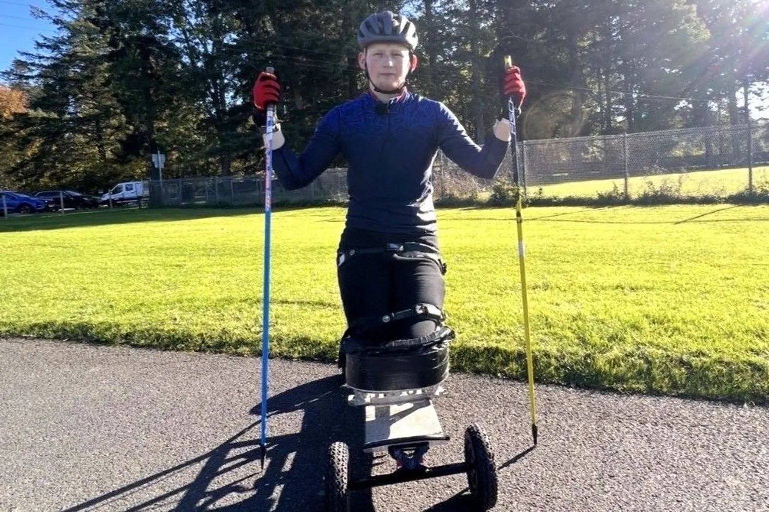 Adam Golebiewski, a young man who has lost both legs, on a board with wheels which allows him to ski, and he is holding ski poles.