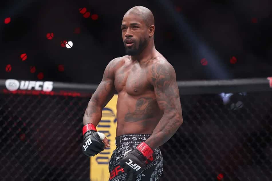 Lutador de UFC com torso tatuado, luvas vermelhas e shorts pretos, dentro da jaula.