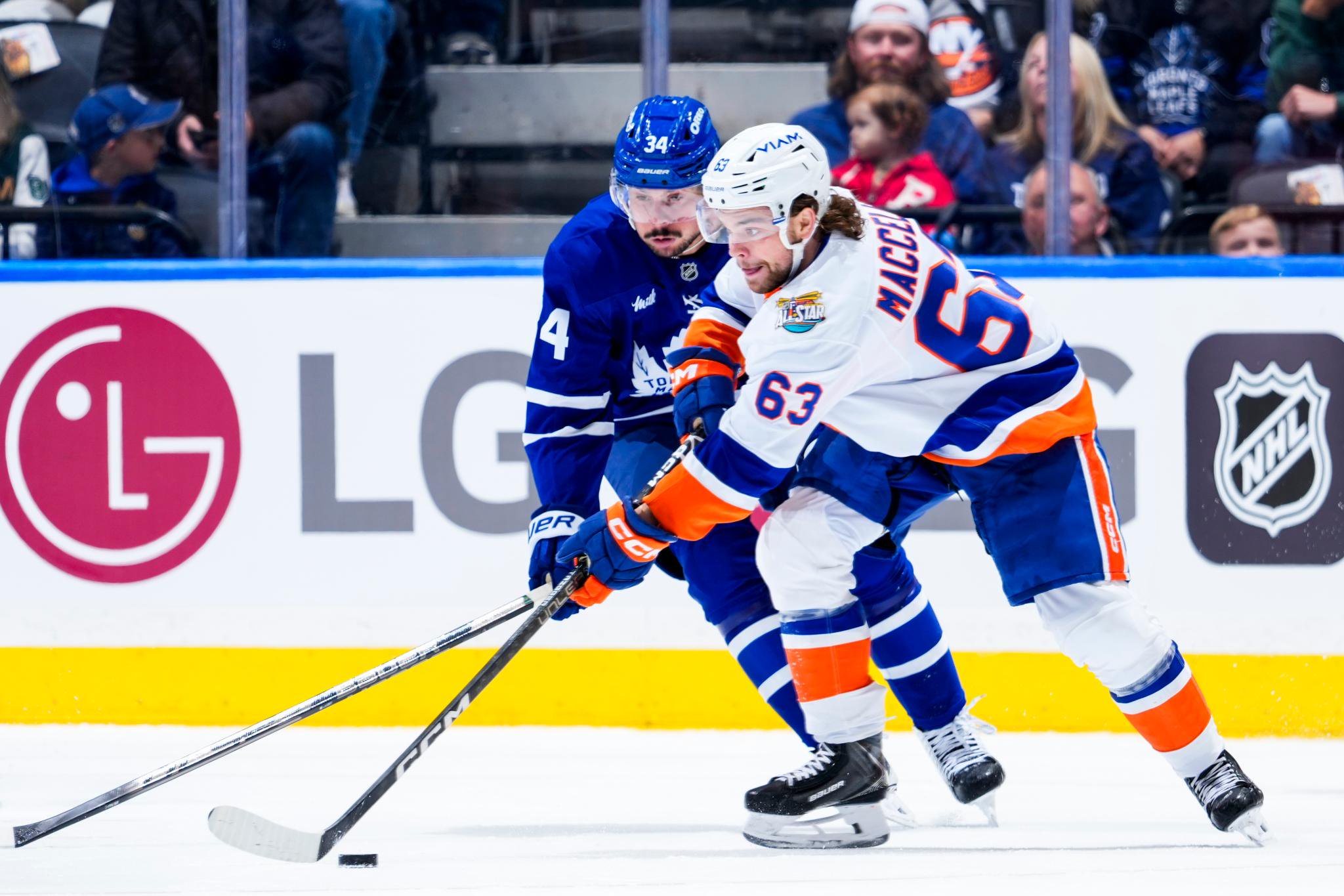 Matias Maccelli of the New York Islanders battles for the puck against Auston Matthews of the Toronto Maple Leafs.