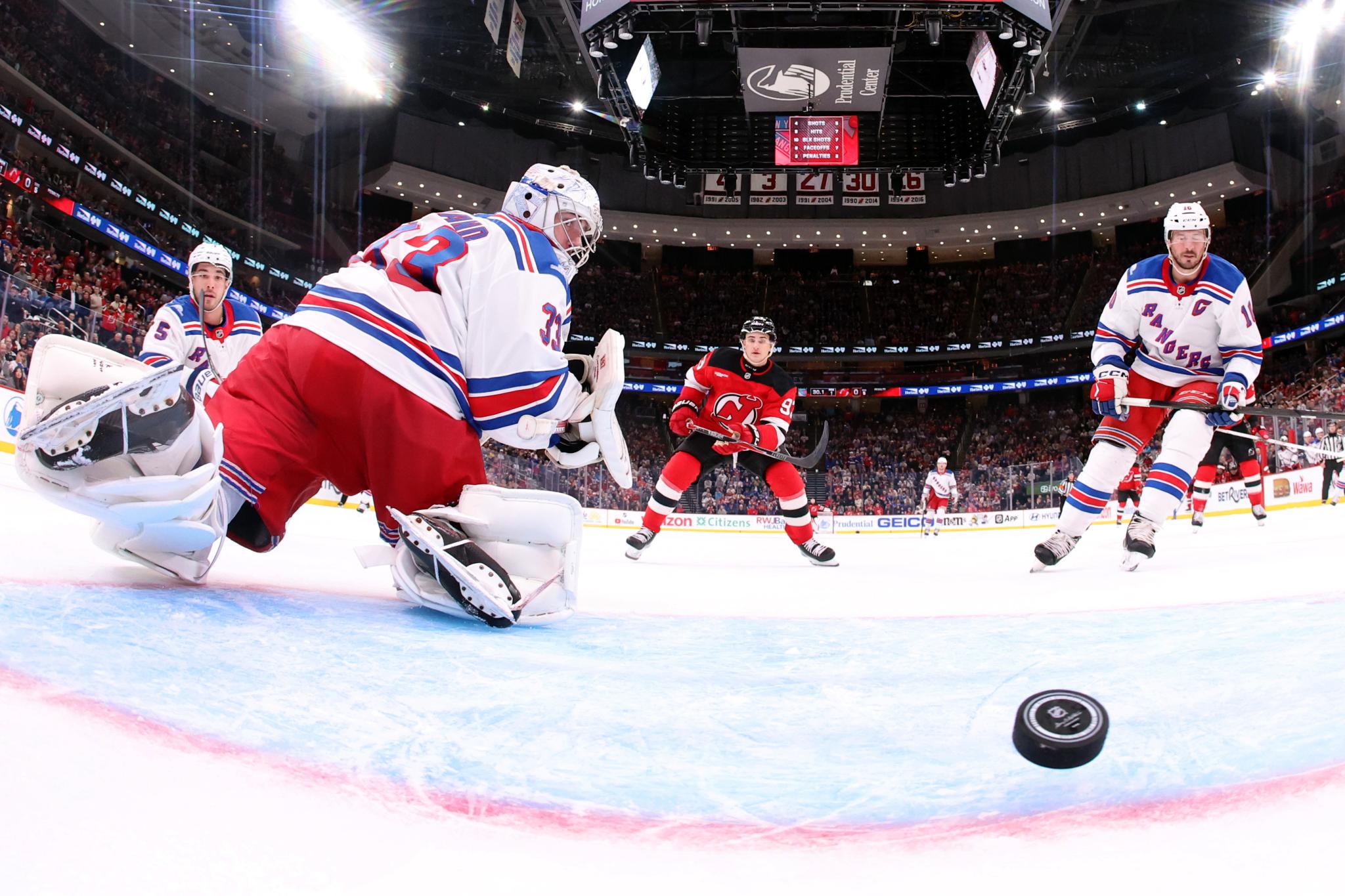 Dylan Garand (33) and J.T. Miller (10) of the New York Rangers look on as Amadeus Lombardi (93) of the New Jersey Devils reacts to a goal scored by Evan Rodrigues (not pictured) on October 15, 2026 in Newark, New Jersey. The Devils won 7-1. 