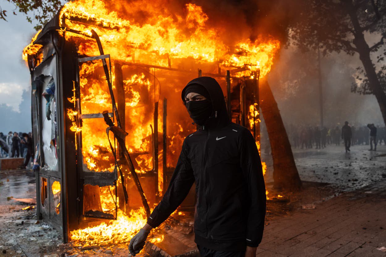 A protester walks past a burning news-stand during demonstrations on October 17, 2026 in Paris, France