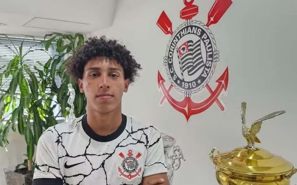 Reginaldo, camisa branca com padrão rachado e emblema do Corinthians Paulista; ao fundo, troféu dourado.