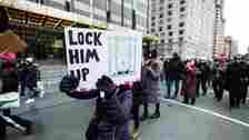 A marcher holds a sight that says "Lock Him Up!"with a picture of President Donald John Trump behind bars the Speaker of the United States House of Representatives who just submitted the articles of Impeachment for President Donald John Trump as she walks in front of Trump International Tower during the Woman's March in the borough of Manhattan in NY on January 18, 2020, USA