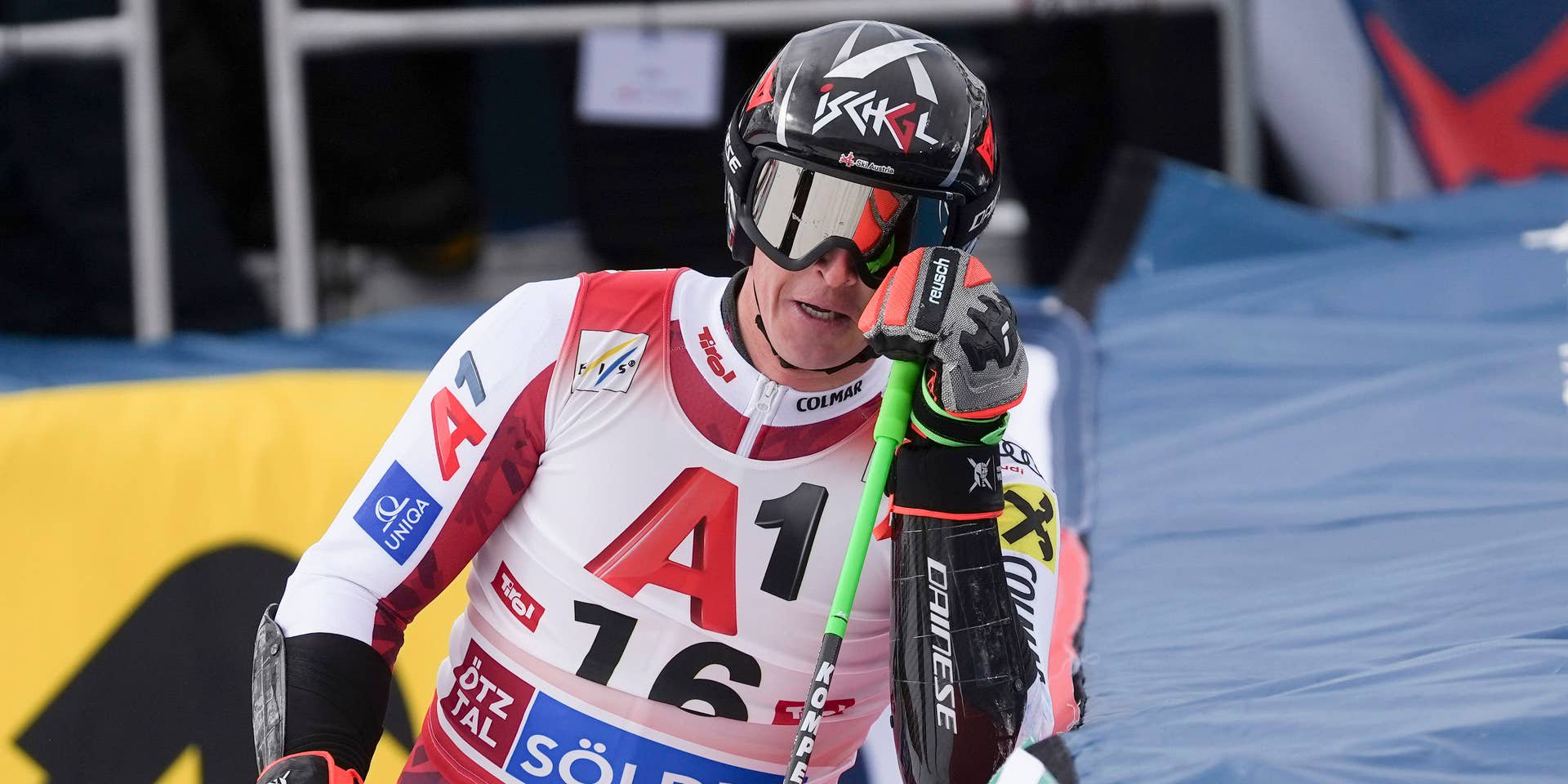 Ein Skifahrer im Rennanzug lehnt sich mit Skistock an die Bande bei einem Riesenslalom-Rennen.
