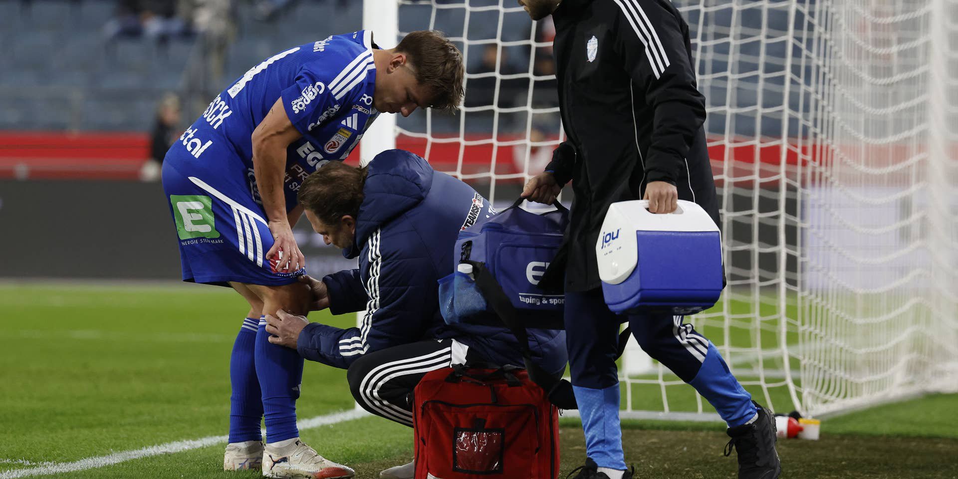 Ein verletzter Fußballspieler wird am Spielfeldrand medizinisch behandelt, neben dem Tor.