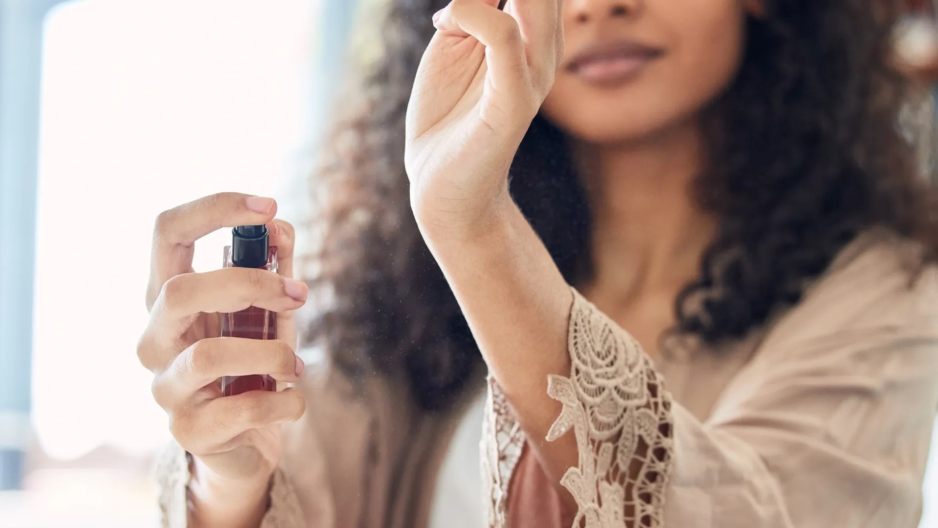 A close up of a woman spraying perfume on her wrists