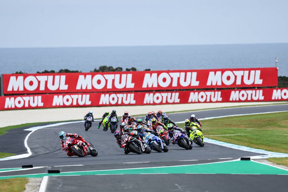 MotoGP pack racing at Phillip Island, a red rider in front on a Ducati, Motul banners behind, sea in background