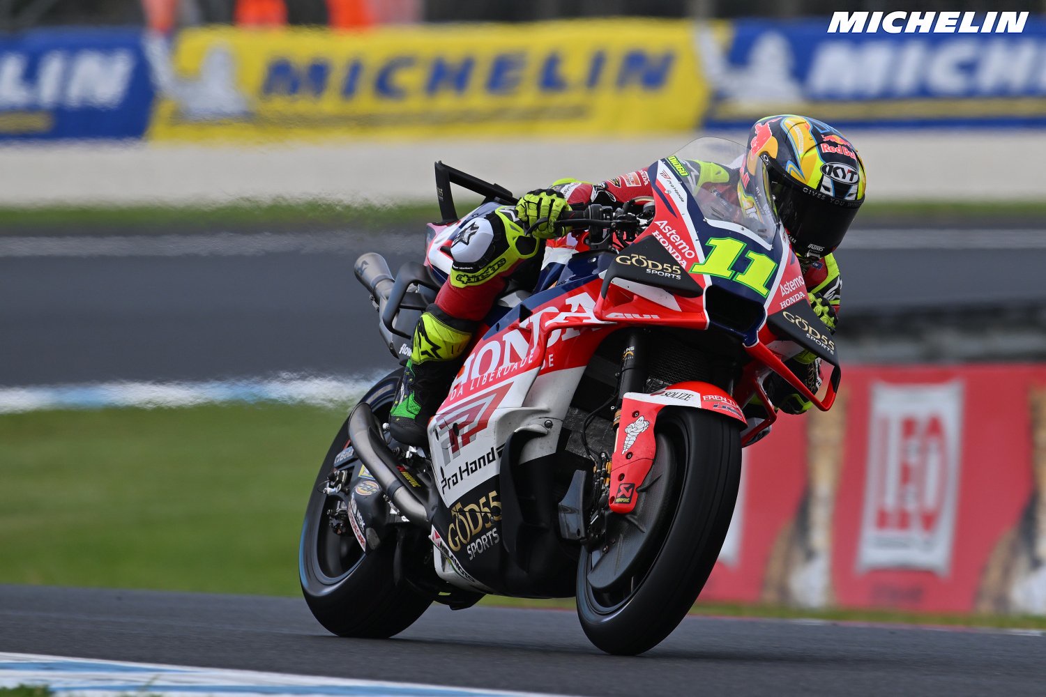 Rider number 11 on a Honda Pro Honda MotoGP bike leaning into a corner at a Michelin-sponsored track, red and white leathers with Gresini-style livery