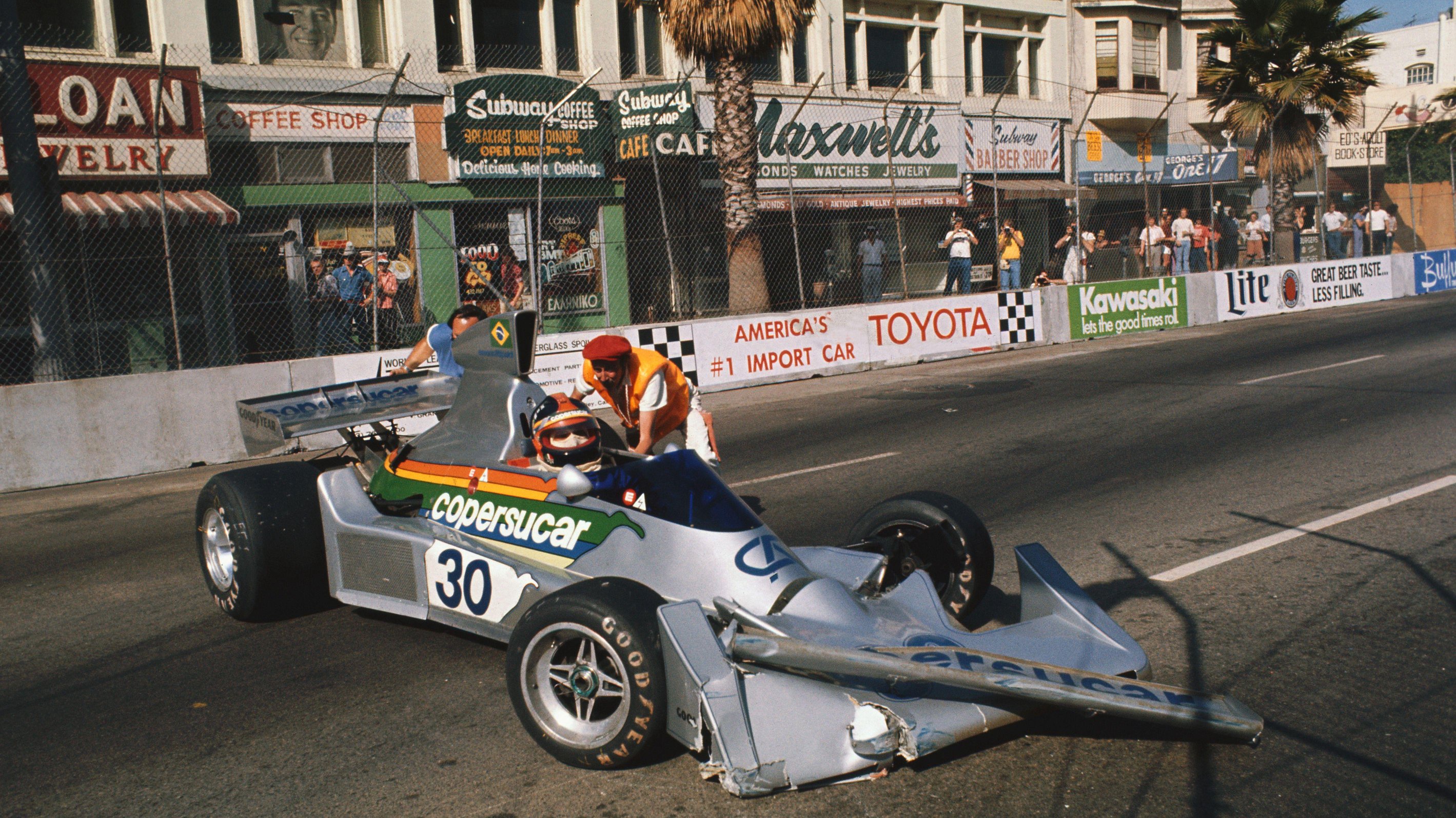 A marshal attends to the Fittipaldi of Emerson Fittipaldi after he crashed in practice for the 1976 Long Beach Grand Prix 