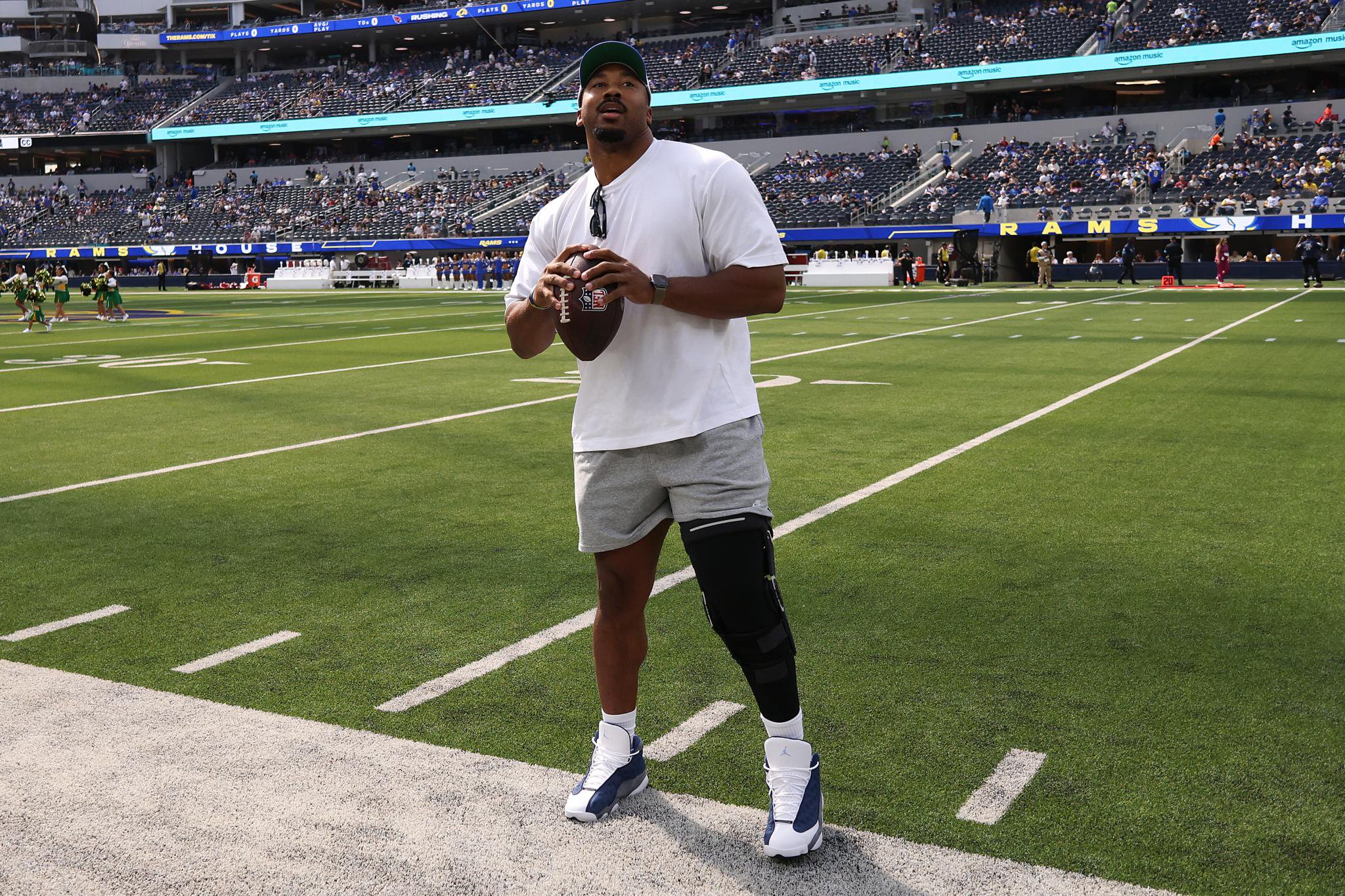 A male football player holding a football and wearing a knee brace on the field.