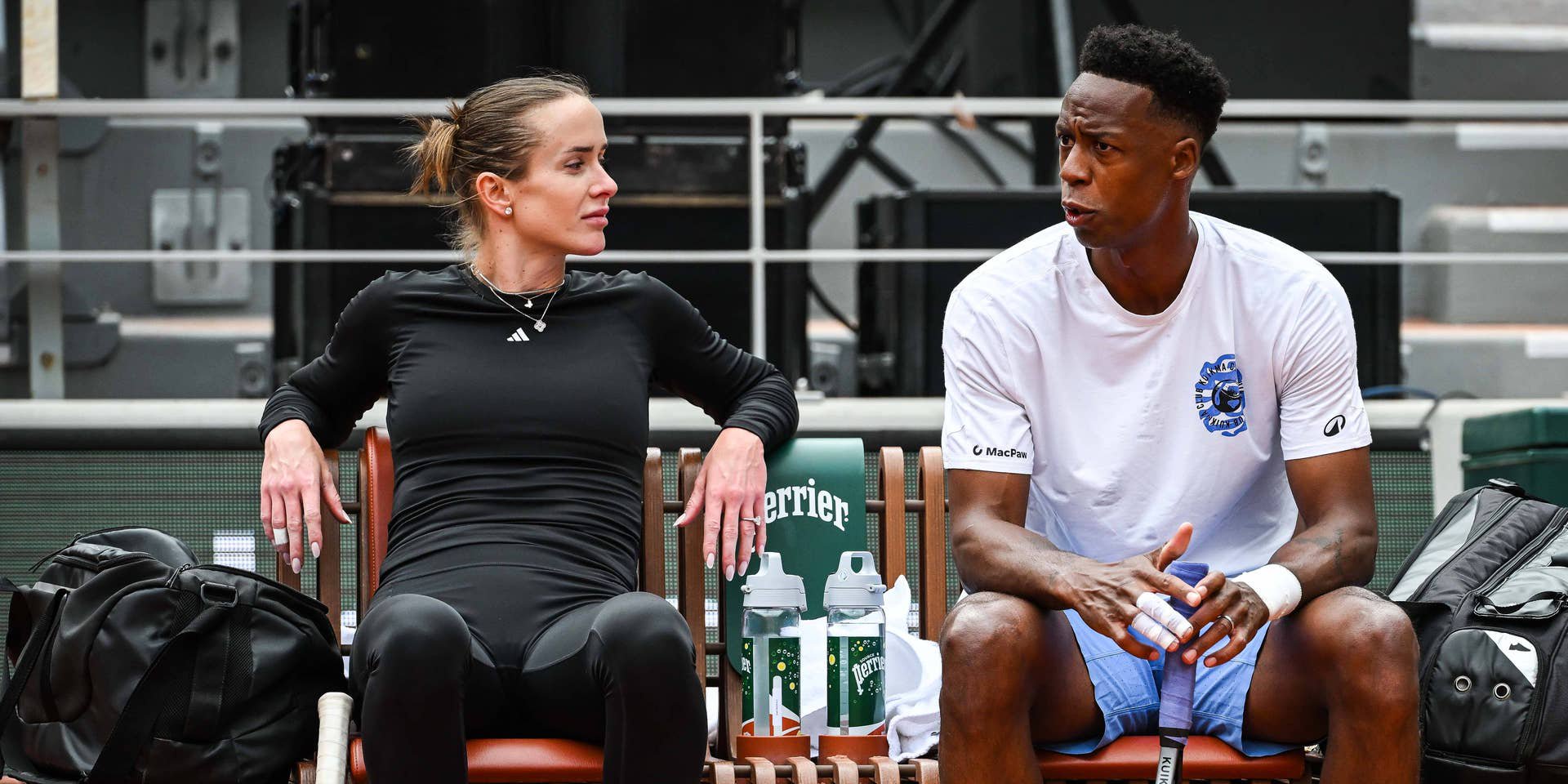 Zwei Tennisspieler sitzen auf einer Bank am Spielfeldrand und unterhalten sich beim Training.