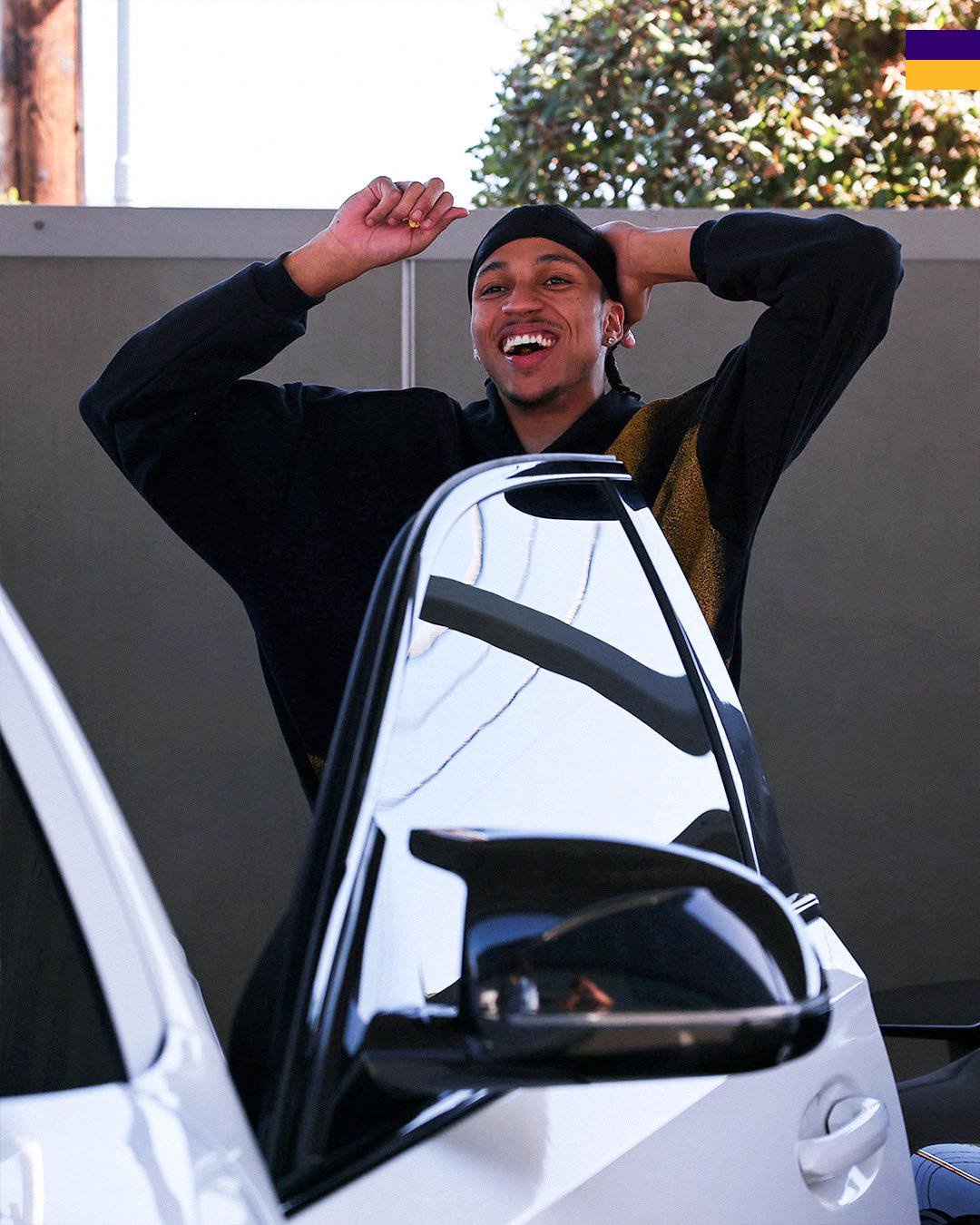 Los Angeles Lakers' Cam Reddish laughing with his hands behind his head next to a car door.