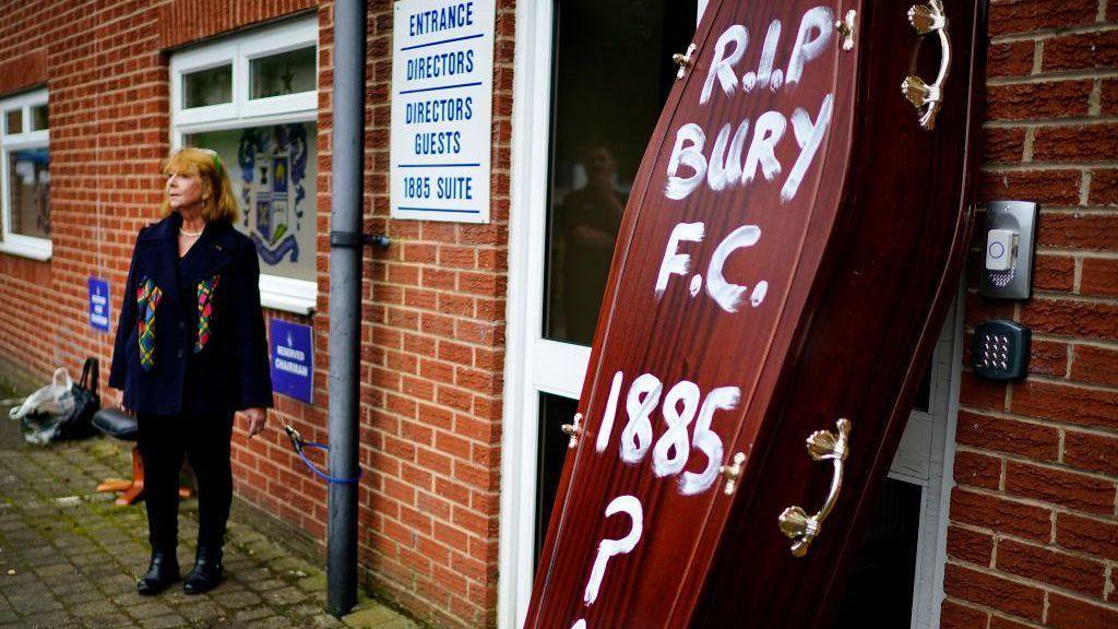 A brown coffin with the words "RIP Bury FC 1885" daubed on it in white paint, propped up outside the club's Gigg Lane ground