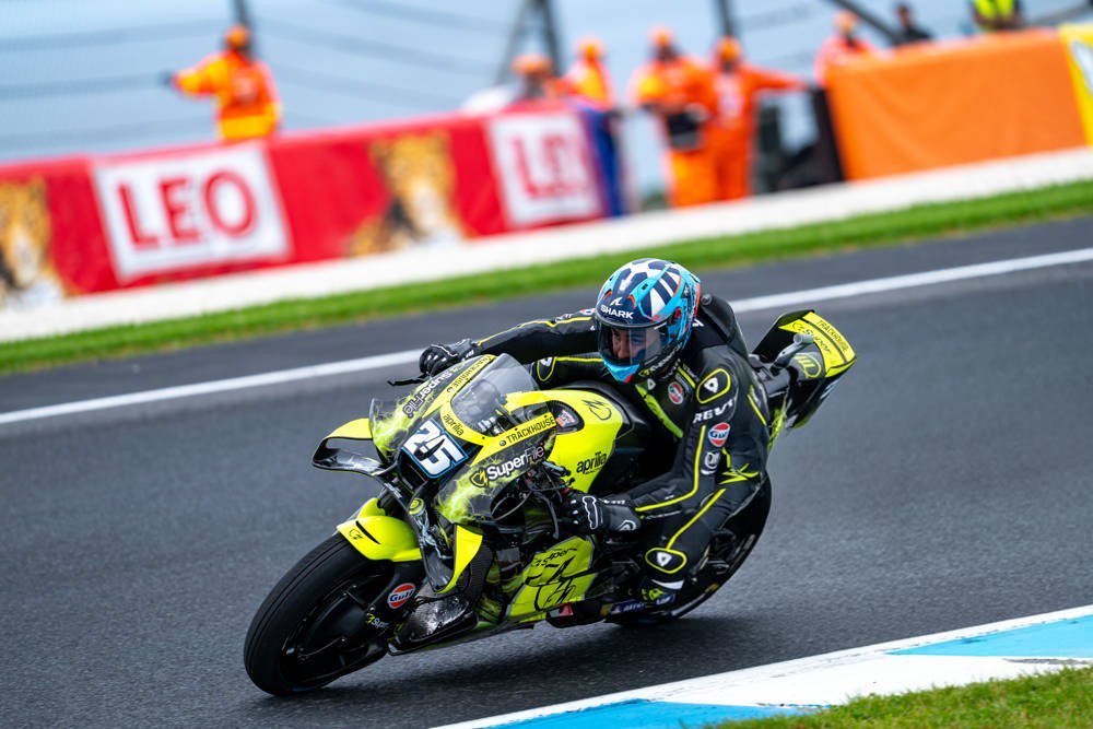 Rider number 25 on a yellow and black Trackhouse-style Aprilia-like MotoGP bike leaning through a corner at the Australian Grand Prix, with a LEO sponsor wal…