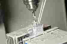 Close-up of a milling machine drilling into a metal workpiece, with coolant fluid spraying around the drill area