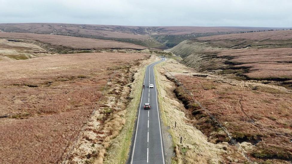 Two cars overtake a cyclist along Snake Pass Summit