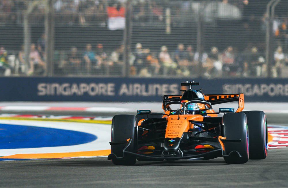 McLaren Formula 1 car in orange livery racing past the Singapore Airlines barrier at a night street circuit