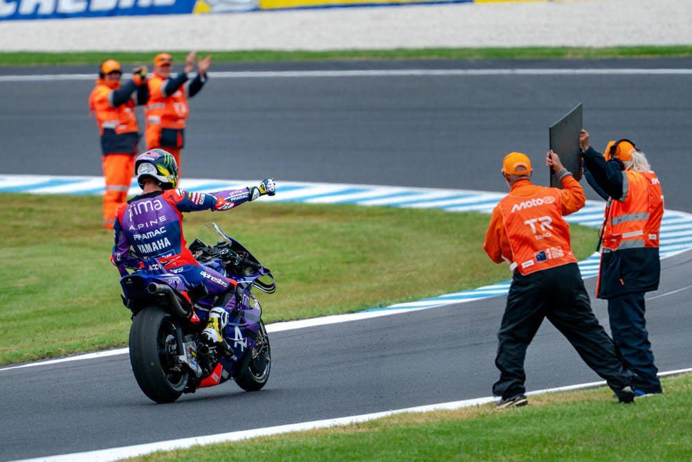Rider in purple and blue Yamaha/Pramac-livery leathers waves on his bike at MotoGP Australia, with marshals in orange applauding trackside.