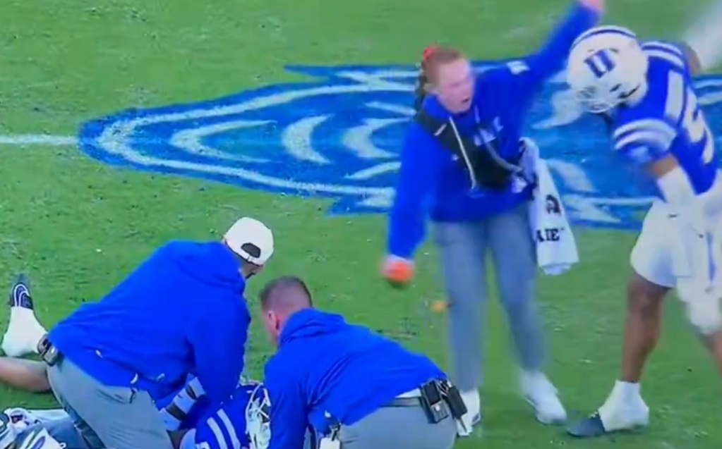 Medical staff and a person in a blue hoodie react as a Duke football player is tended to on the field.