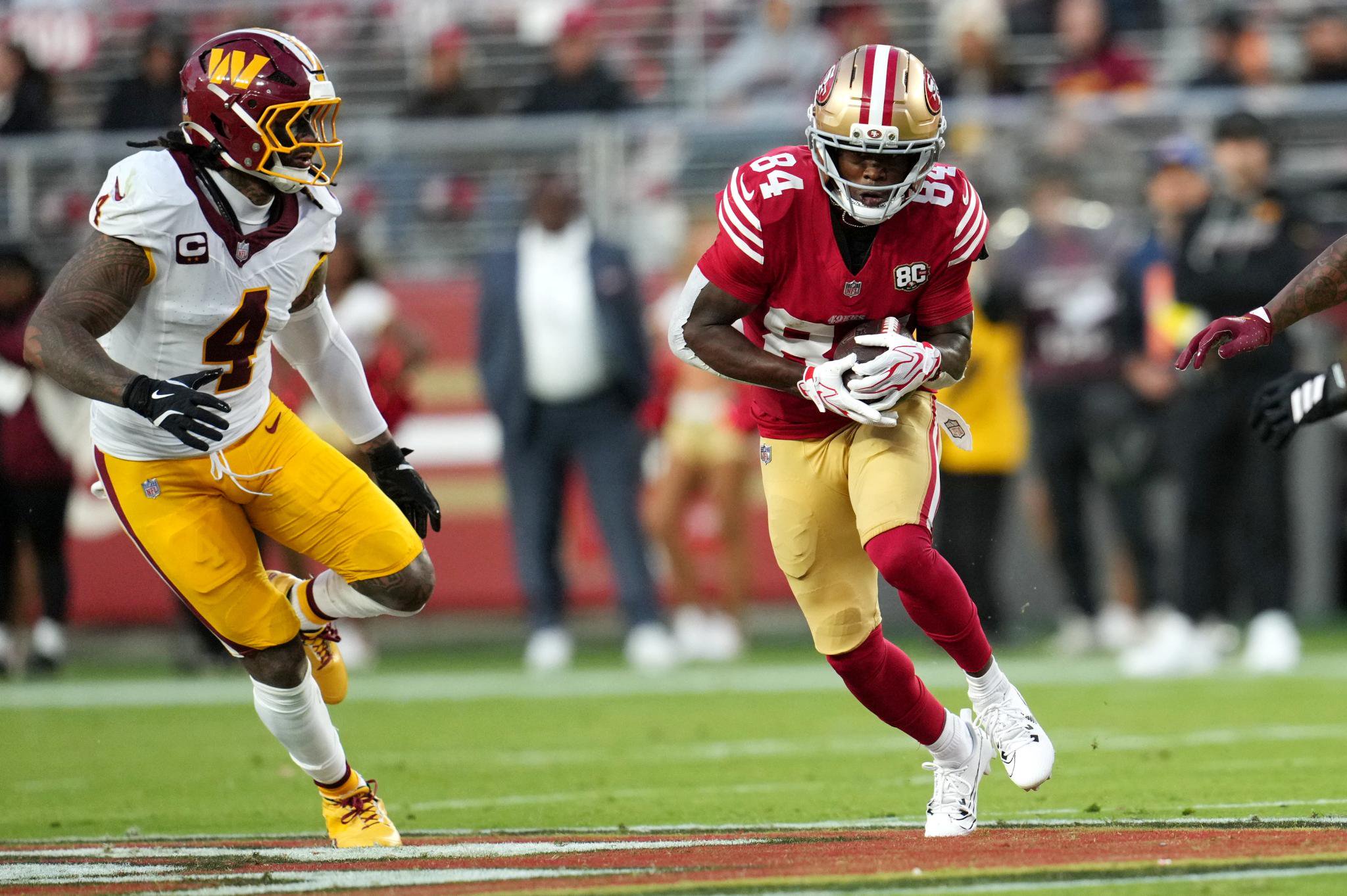 San Francisco 49ers wide receiver Deebo Samuel runs with the ball while pursued by Washington Commanders defender Darrick Forrest during a game.