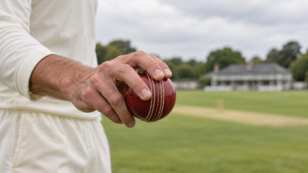 Adult cricketer holding a red ball beside the pitch