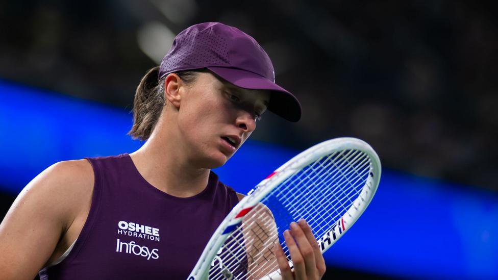 Iga Swiatek, in purple sleeveless tennis top and purple cap, looks at her racquet during a Wuhan Open semi-final defeat