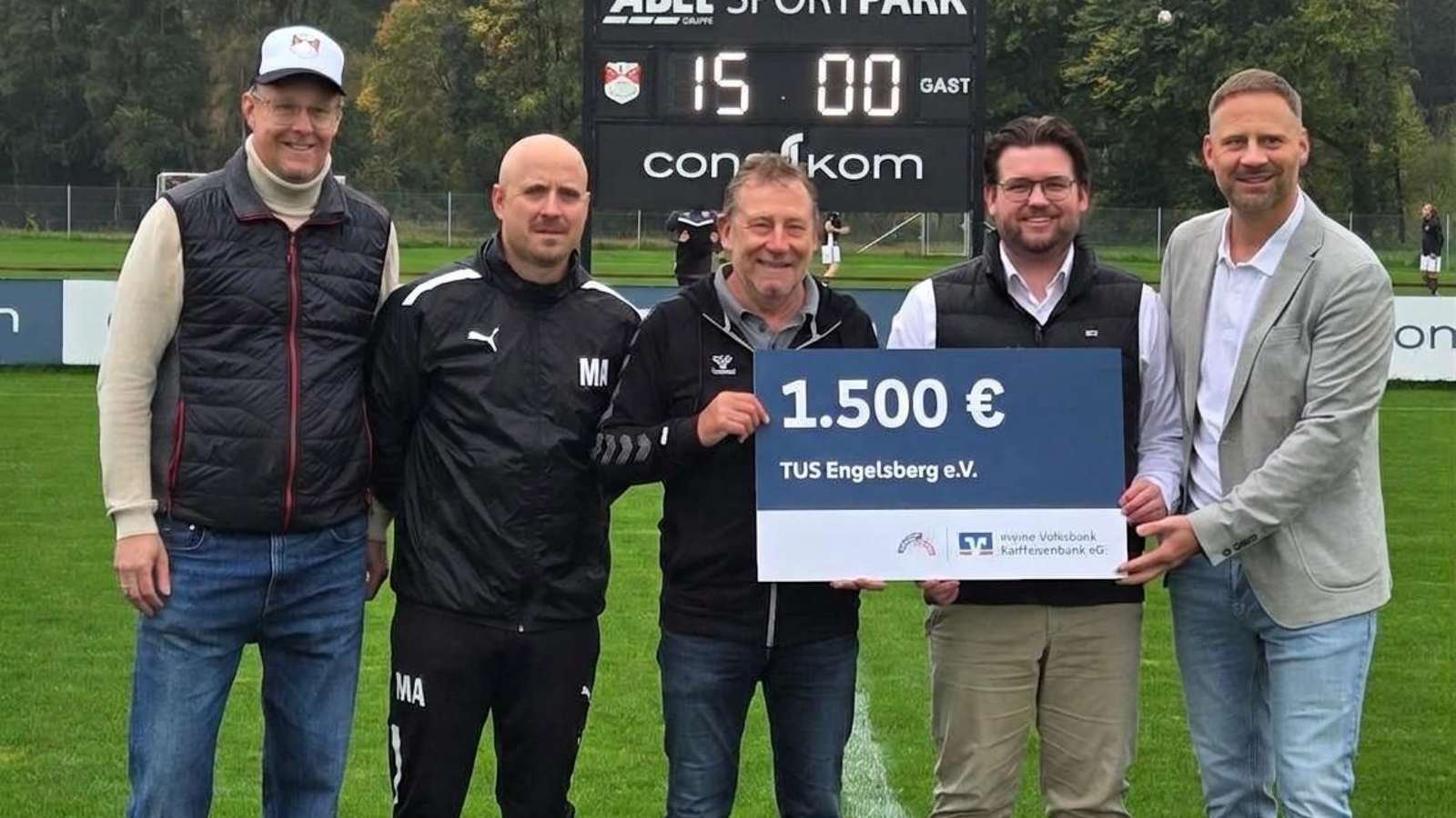 Fünf Männer bei der Spendenübergabe eines 1.500-Euro-Schecks der VR-Bank an die Fußballabteilung des TuS Engelsberg auf dem Sportplatz