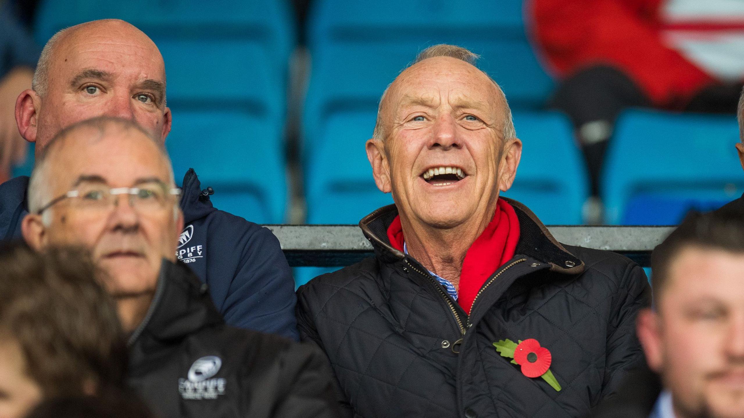 Lyndon Faulkner sits among other spectators and wears a red scarf and dark coat