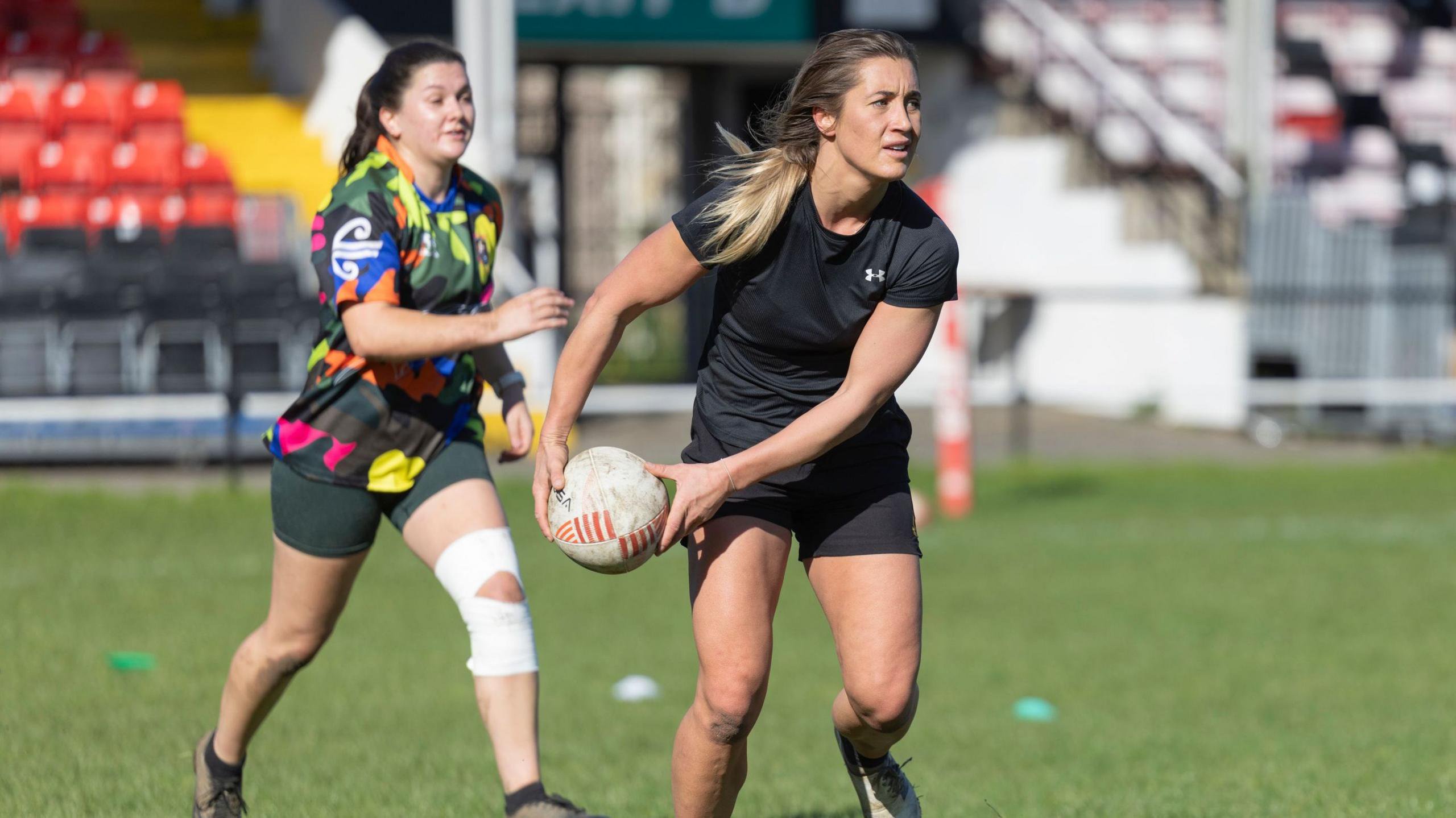 Paige Randall (foreground) wearing all black rugby kit is about to throw the ball during a training exercise while Theo Rushton runs behind her during a Wales Deaf Rugby session.