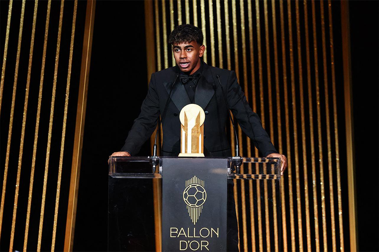 Lamine Yamal speaks at the Ballon d'Or ceremony behind a podium bearing the award's logo.