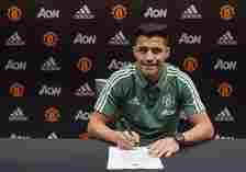 Alexis Sanchez sits at a table and signs his Manchester United contract.