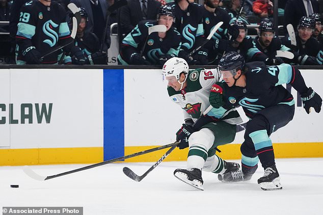 Minnesota Wild center Tyler Pitlick, left, and Seattle Kraken defenseman Ryker Evans, right, grapple for position as they chase the puck during the third period of an NHL hockey game Saturday, Oct. 24, 2026, in Seattle. (AP Photo/Lindsey Wasson)
