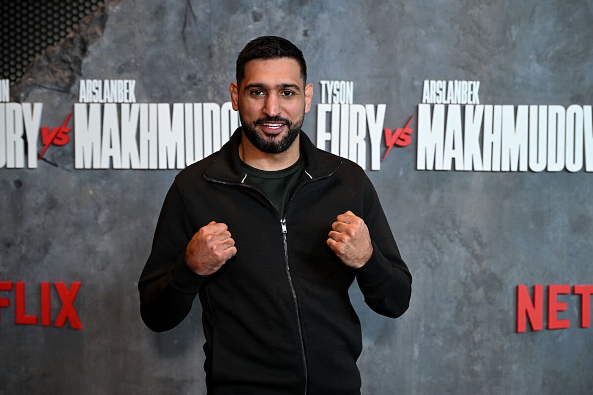 Amir Khan, former boxing champion, clenches fists in front of a Fury vs Makhmudov promotional backdrop