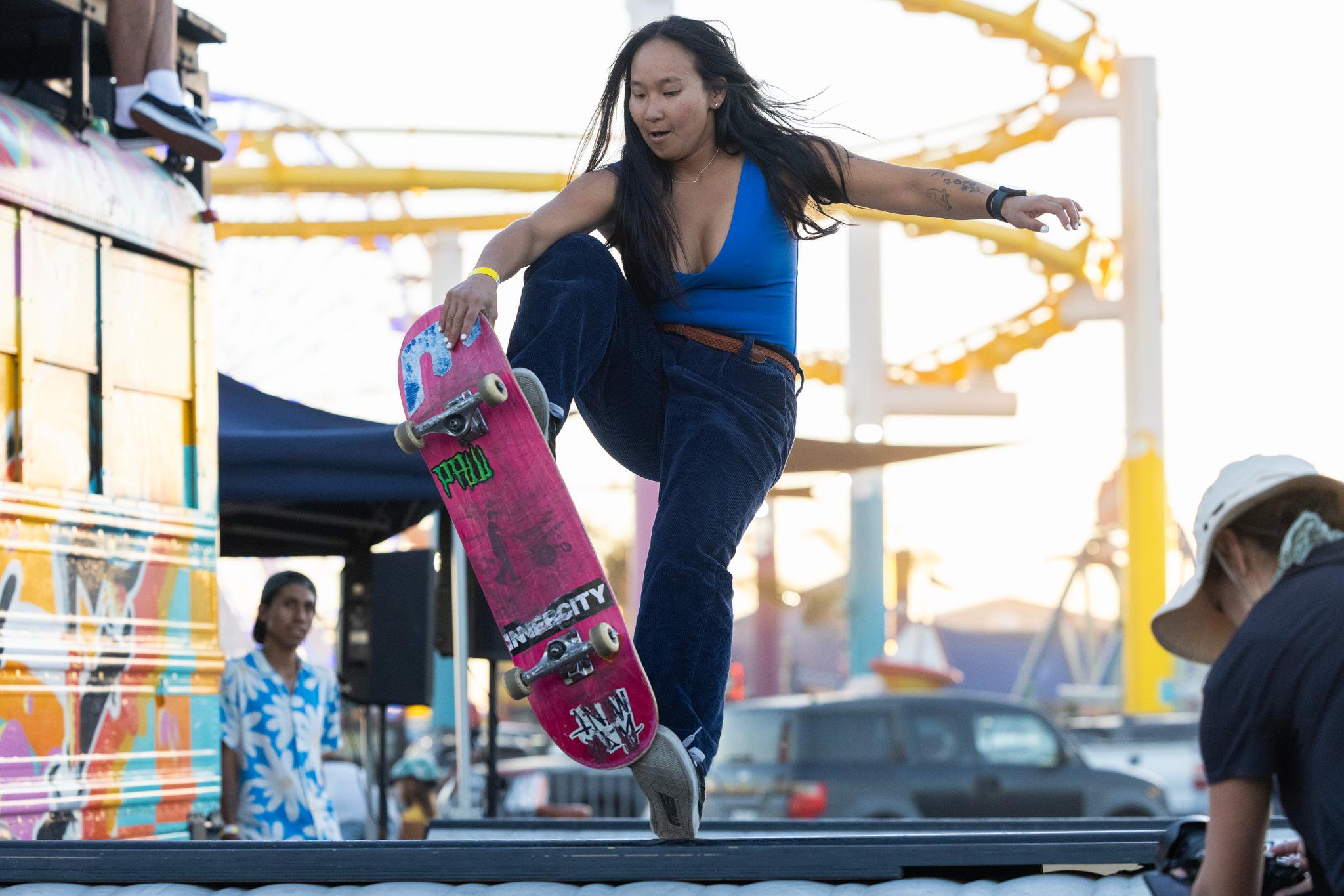A skateboarder performs a trick with a pink skateboard on the Santa Monica Pier.