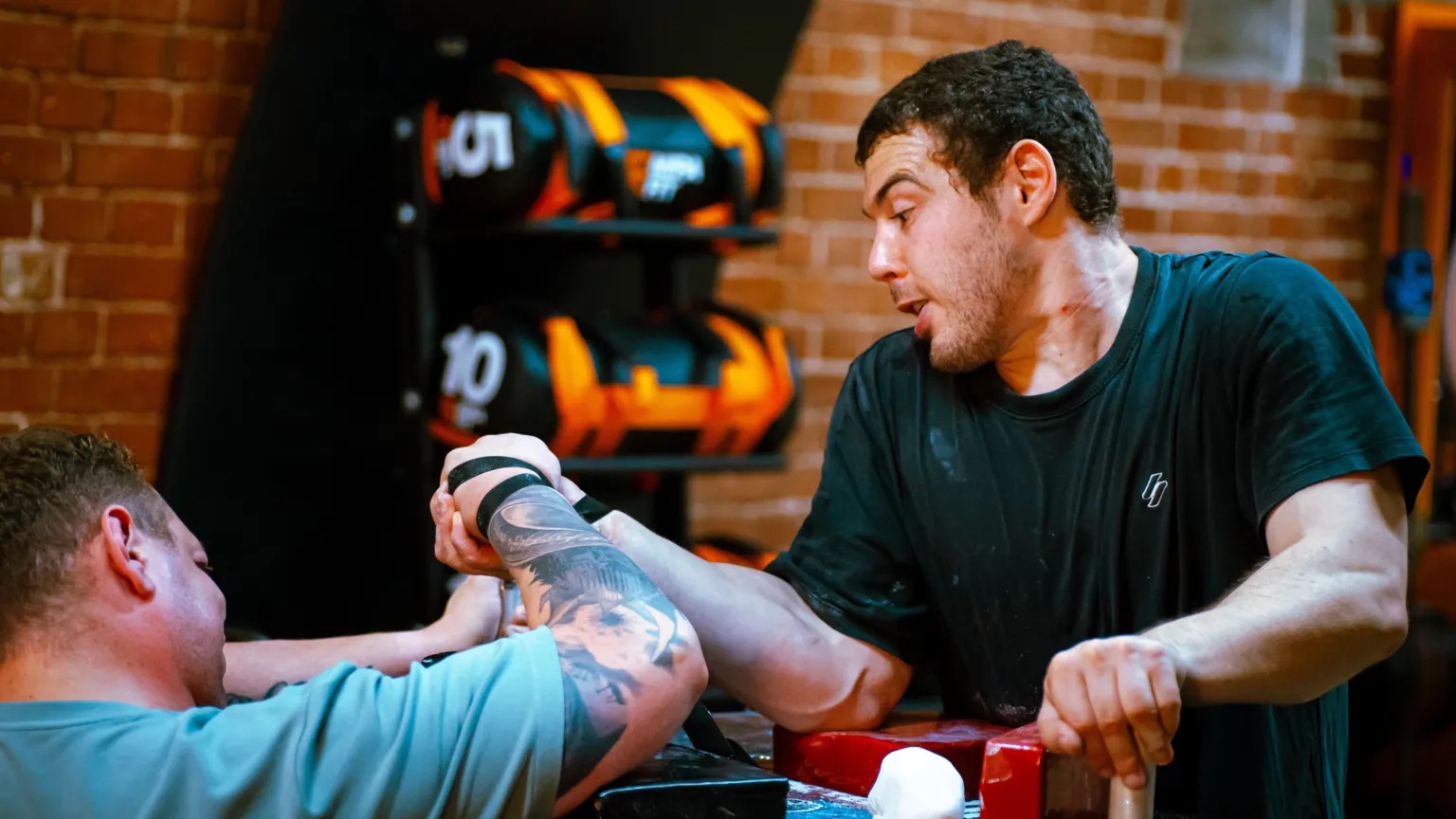 Suffolk Arm Wrestling Team Two men arm wrestle in a gym. One of the men has managed to move down the other's arm.