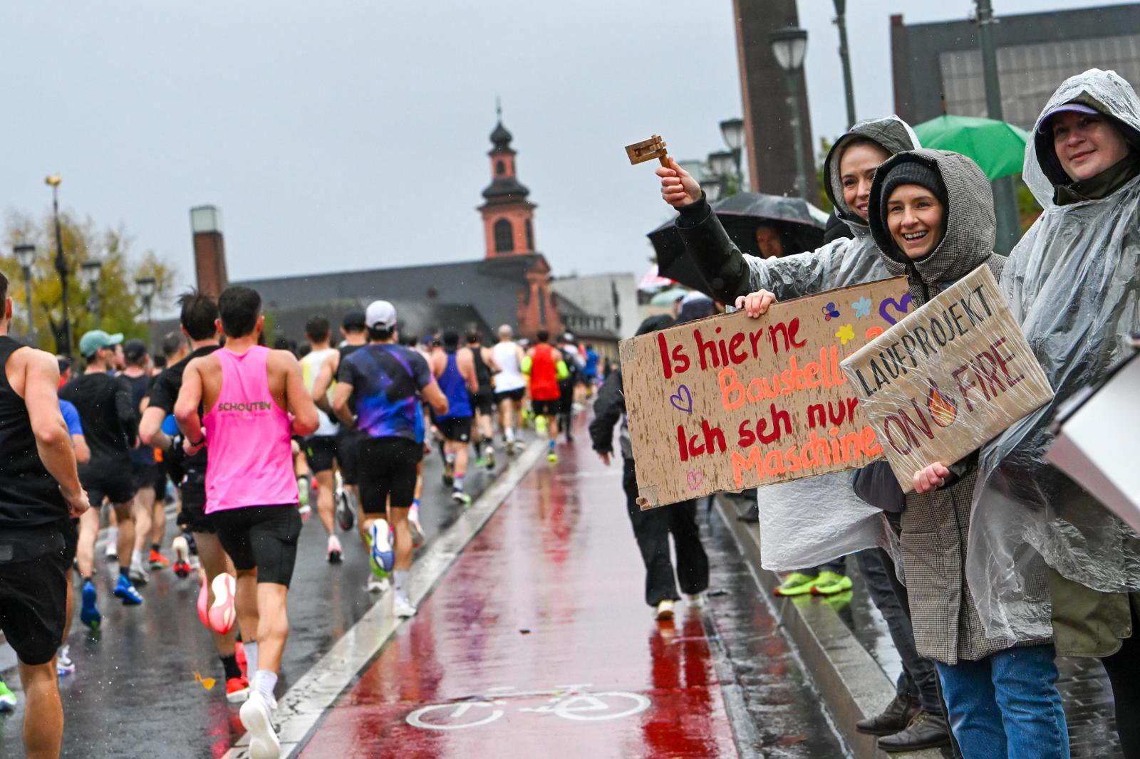 Der erste Teil der Laufstrecke in stroemendem Regen. Zuschauer auf und vor der Alten Bruecke, mit Schirmen und wetterfester Kleidung, feuern die Laeufer an.