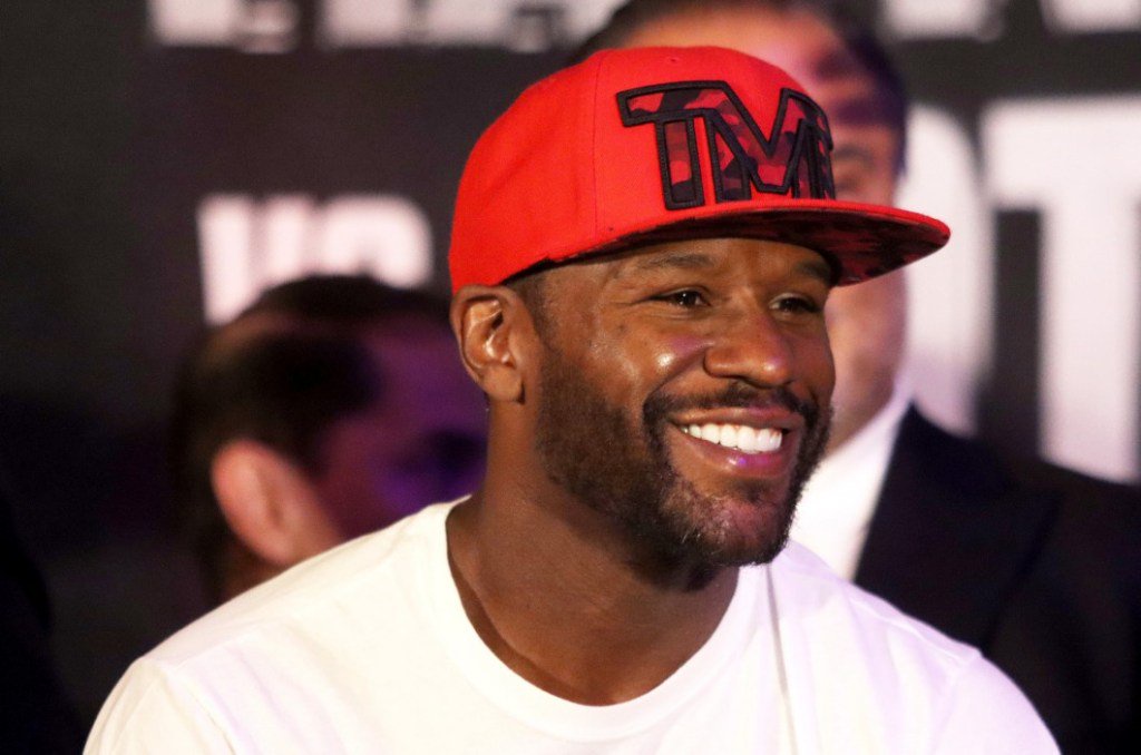 Floyd Mayweather Jr. smiling while wearing a red baseball cap and white t-shirt.