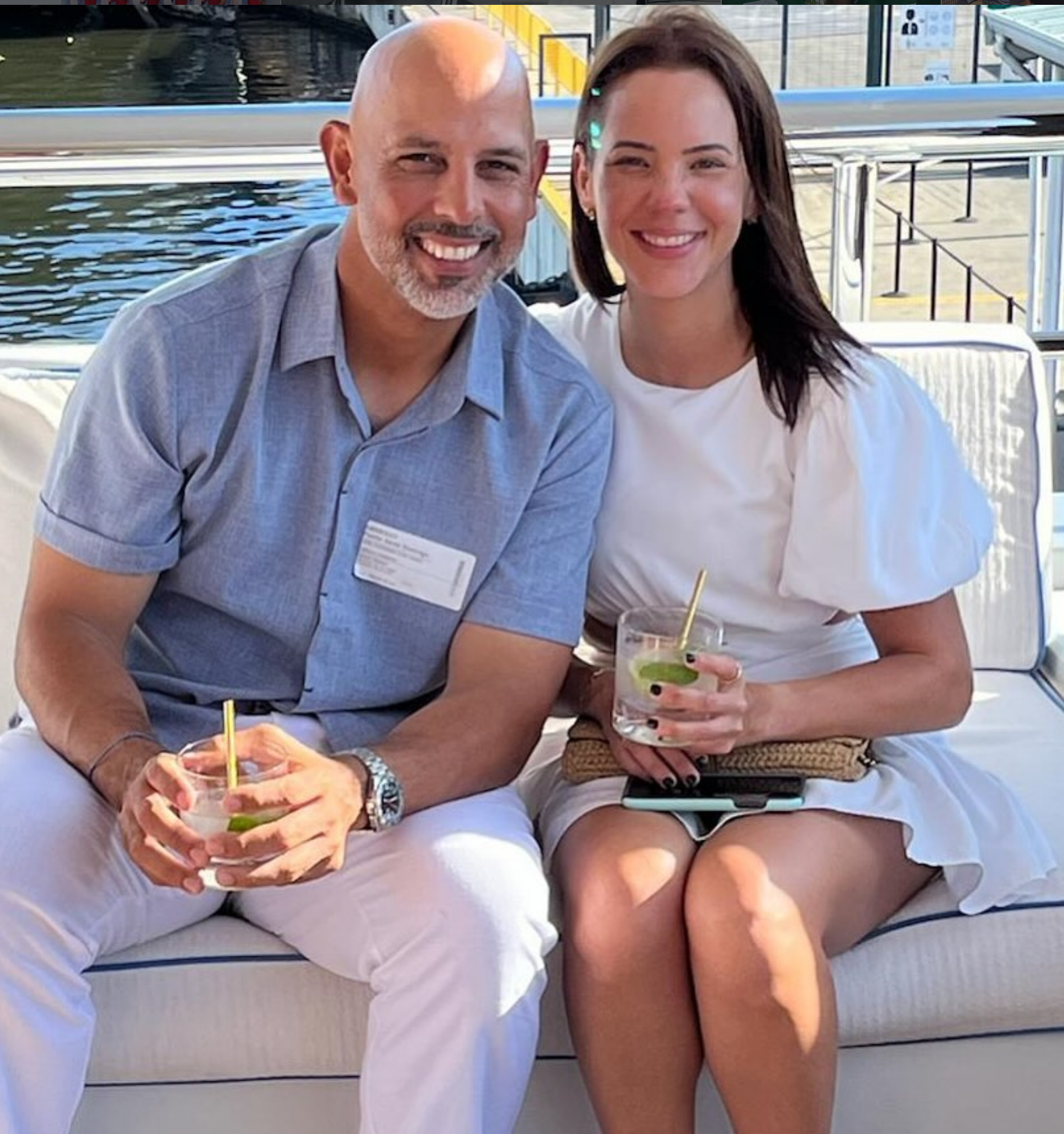 A man and a woman sitting on an outdoor couch while holding drinks with straws.